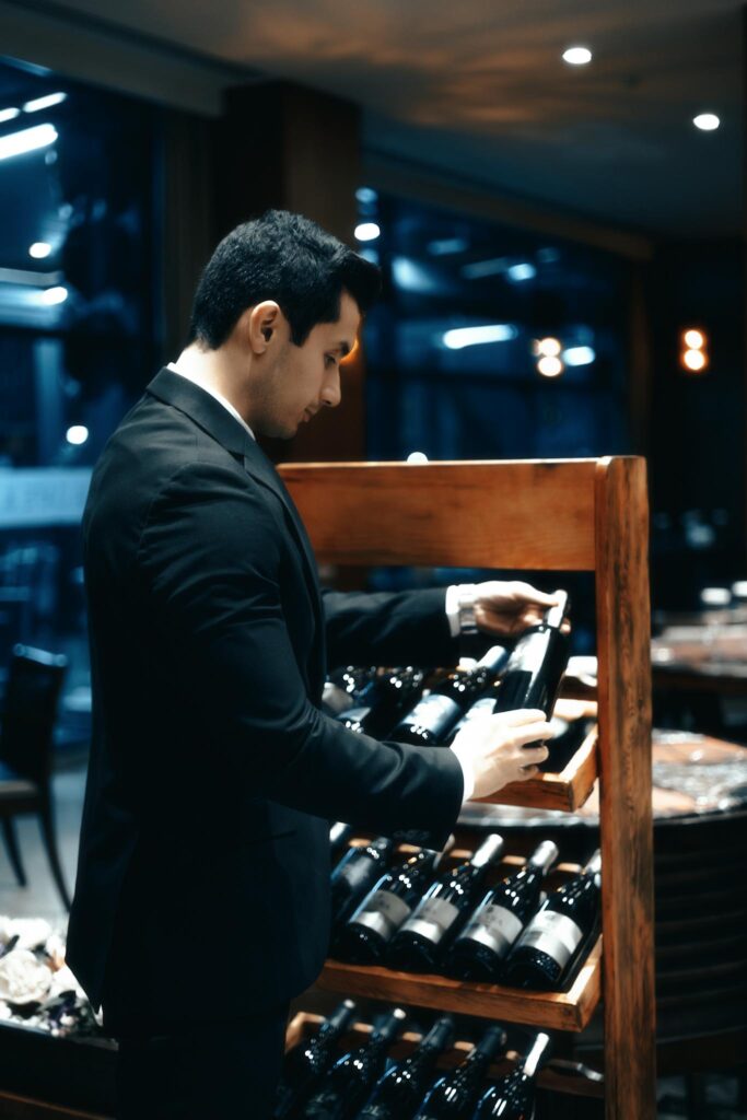 Man in a suit choosing a wine bottle from a shelf in a dimly lit restaurant.