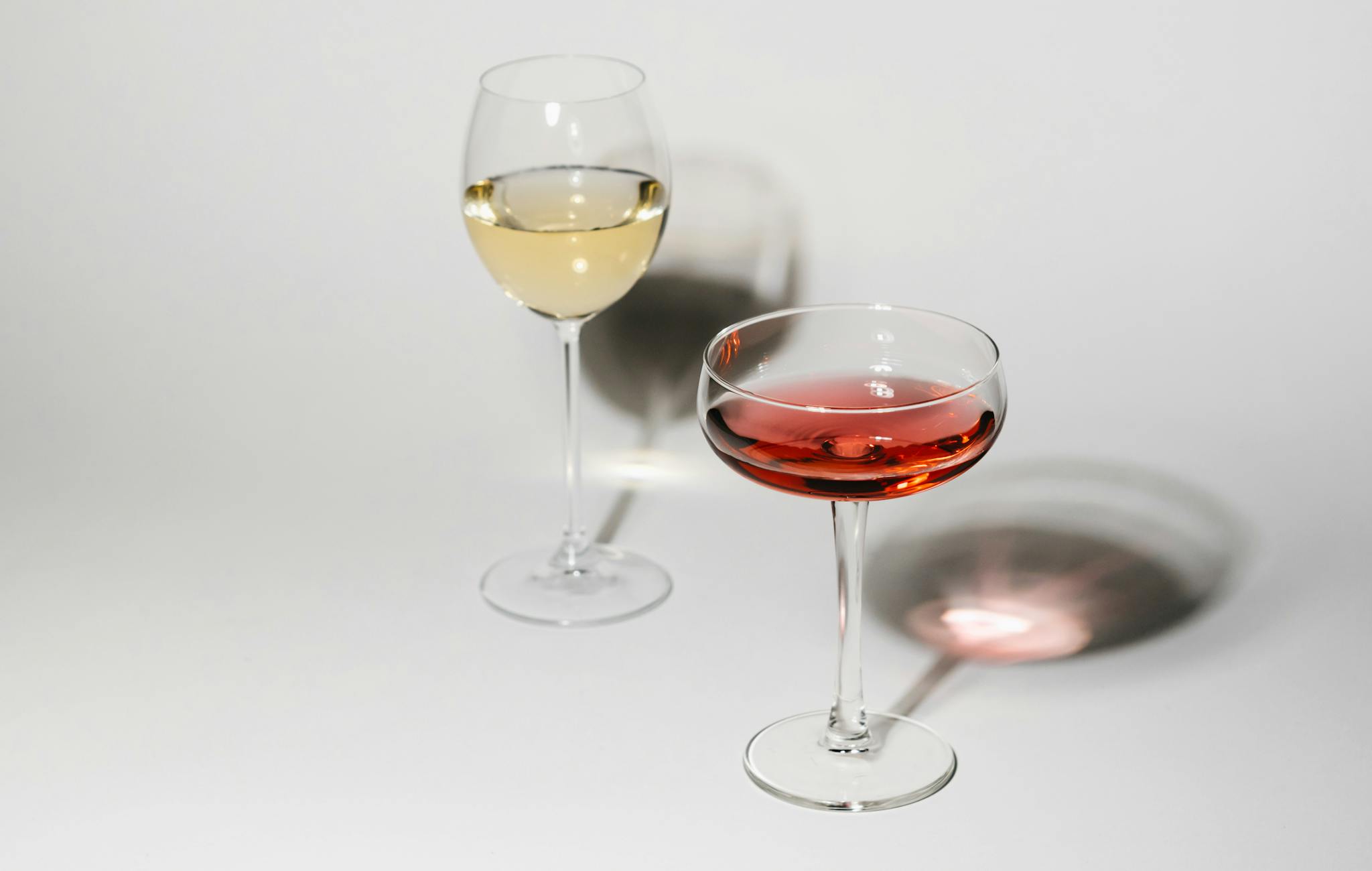 Two wine glasses casting soft shadows on a white background, showcasing red and white wines.